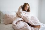 Beautiful cheerful girl covered in blanket smiling and sitting on bed