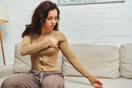 Young brunette woman in brown jumper suffering from pain while massaging lymphatic nodes on armpit